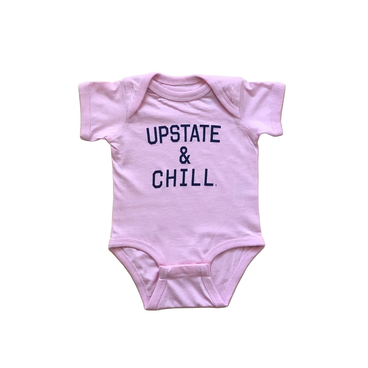 Pink baby onesie with 'UPSTATE & CHILL' text on a wooden surface