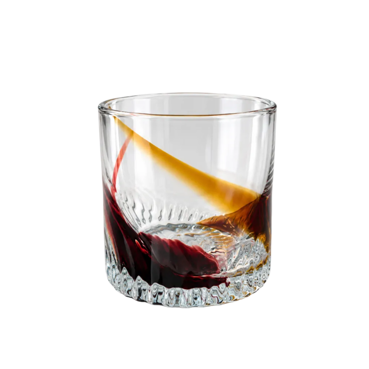 A clear glass rocks tumbler with a textured, faceted base, shown on a white background with a diagonal splash of dark red and amber liquid inside.