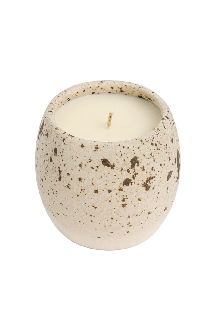 Speckled ceramic candle holder with a lit candle on a white background