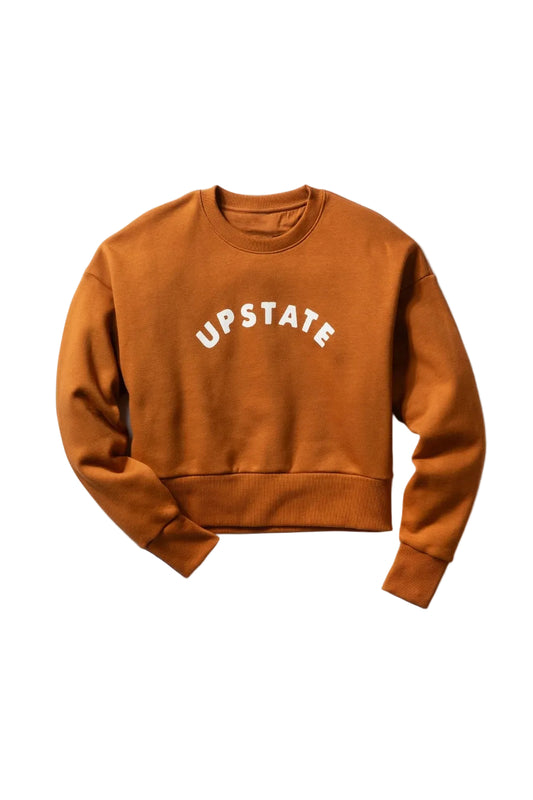 A rust-orange cropped crewneck sweatshirt with 'UPSTATE' printed in white arched text across the chest, displayed flat against a light gray background.