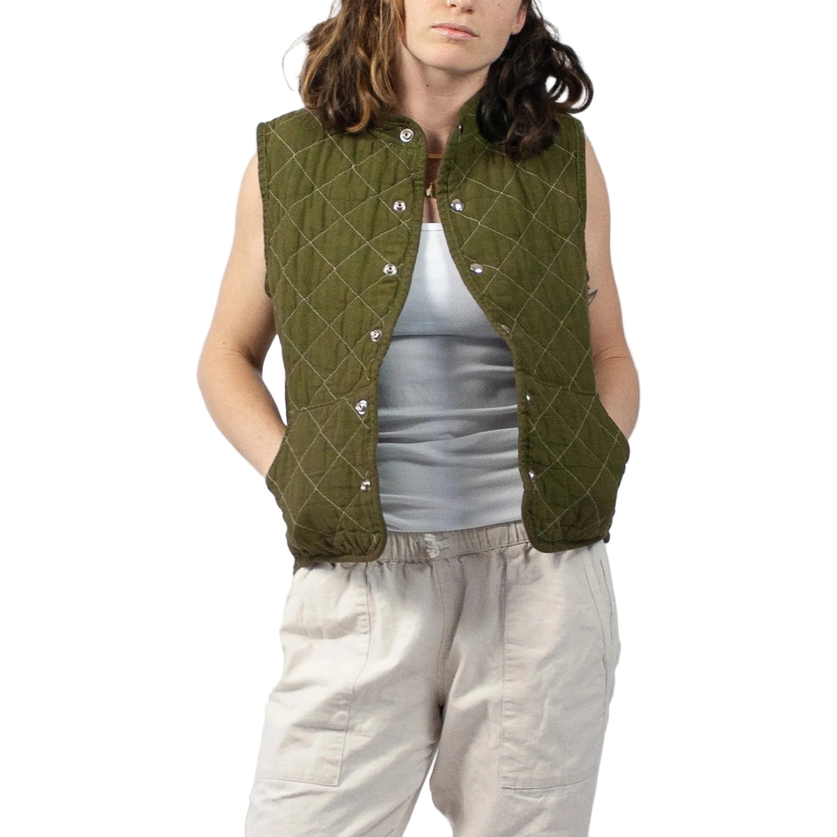 Person wearing a green quilted vest over a gray top and beige pants on a plain background