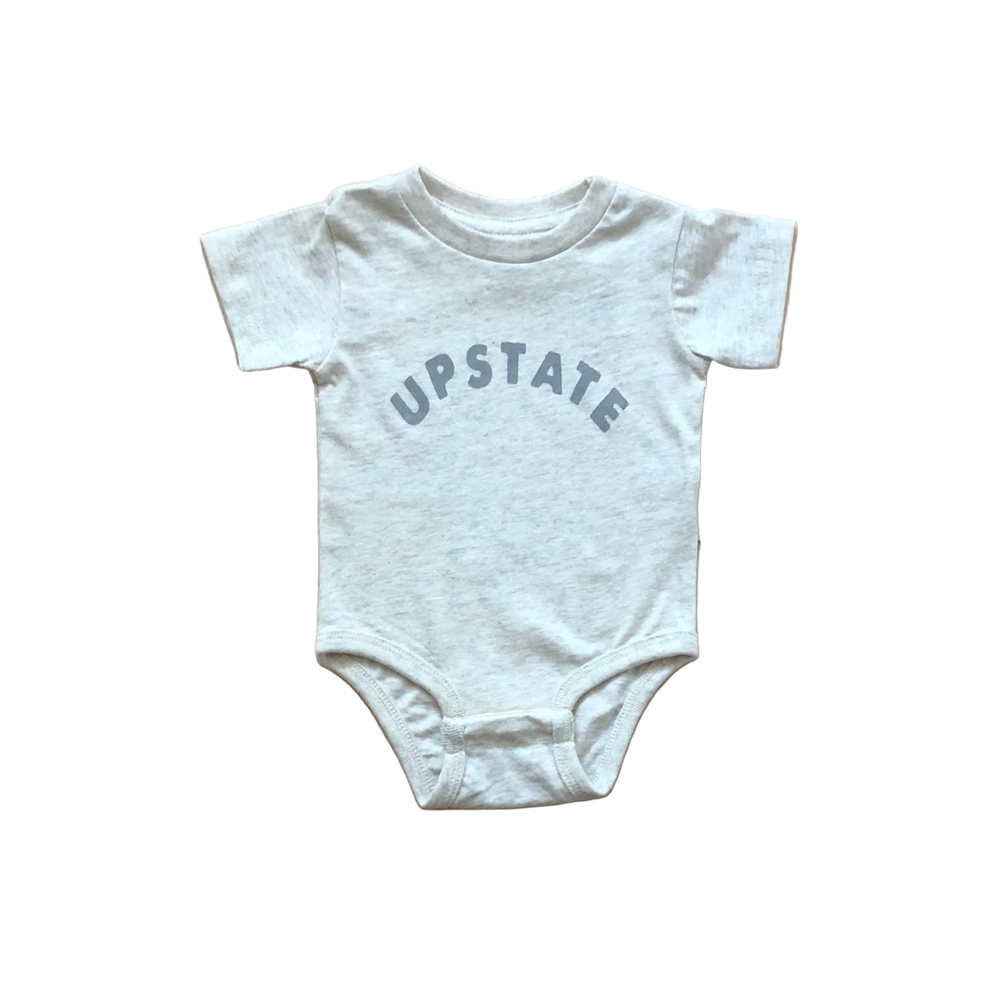 White baby onesie with 'UPSTATE' text on a wooden surface