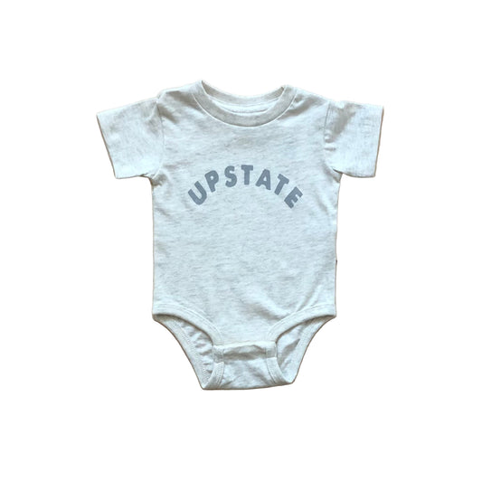 White baby onesie with 'UPSTATE' text on a wooden surface